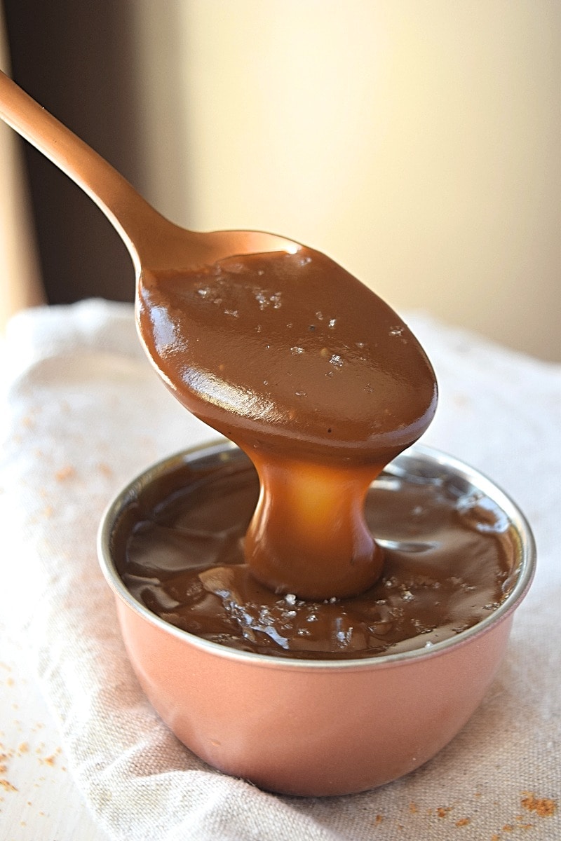 Coconut caramel falling off a spoon int a bowl.