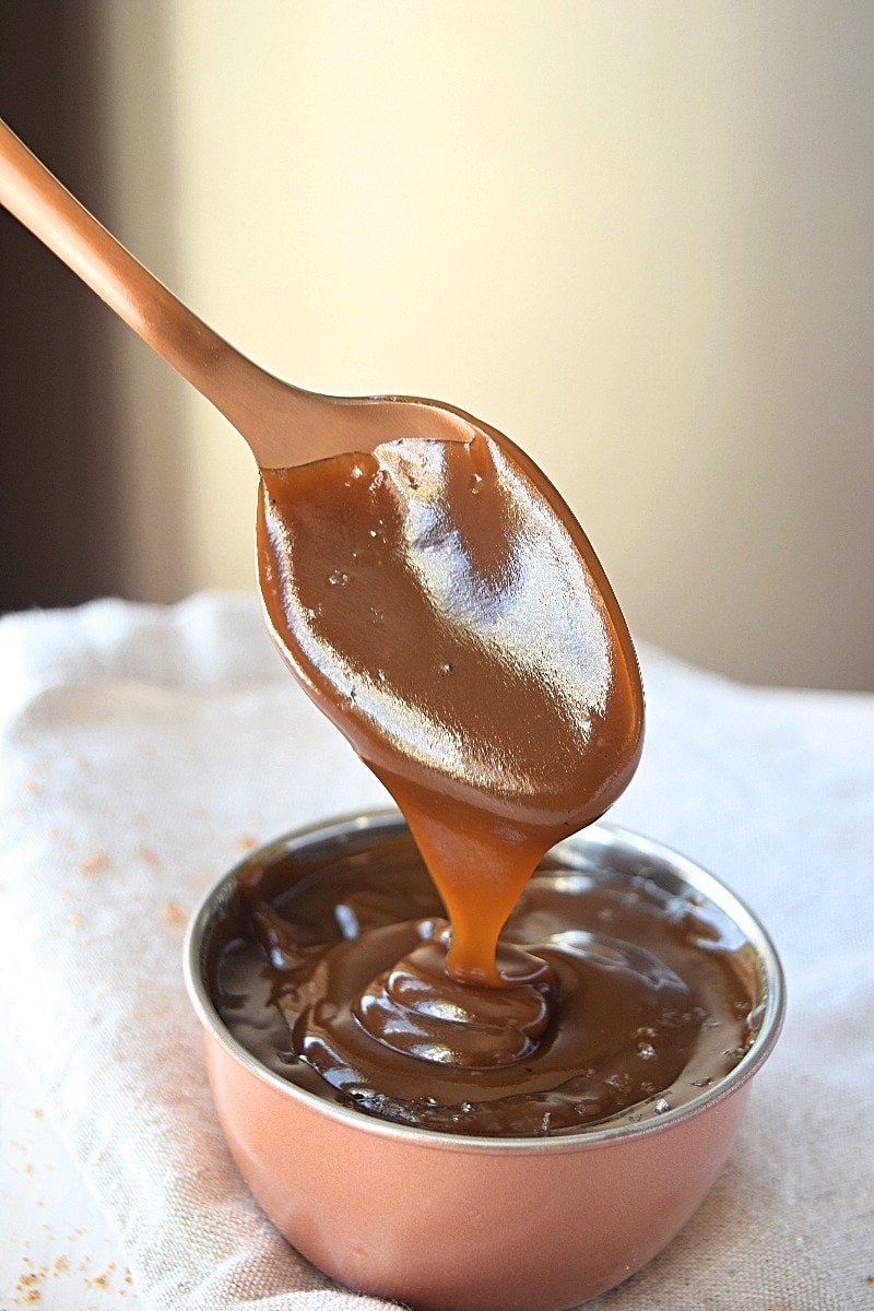 Coconut caramel falling off a spoon int a bowl.