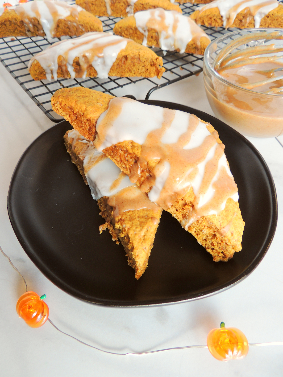 Two freshly baked gluten free pumpkin scones sitting on top of a black plate.