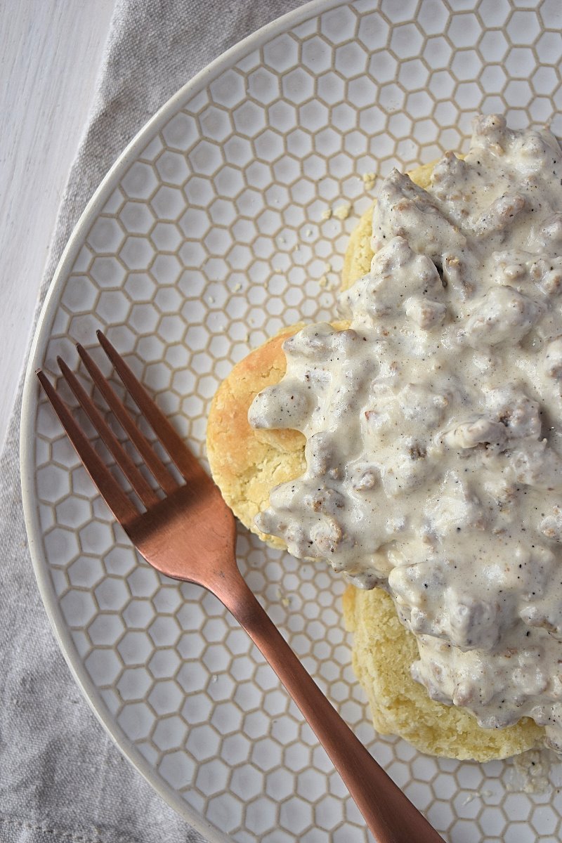 An overhead view of a plate full of biscuits and gravy with a fork beside them on a white plate