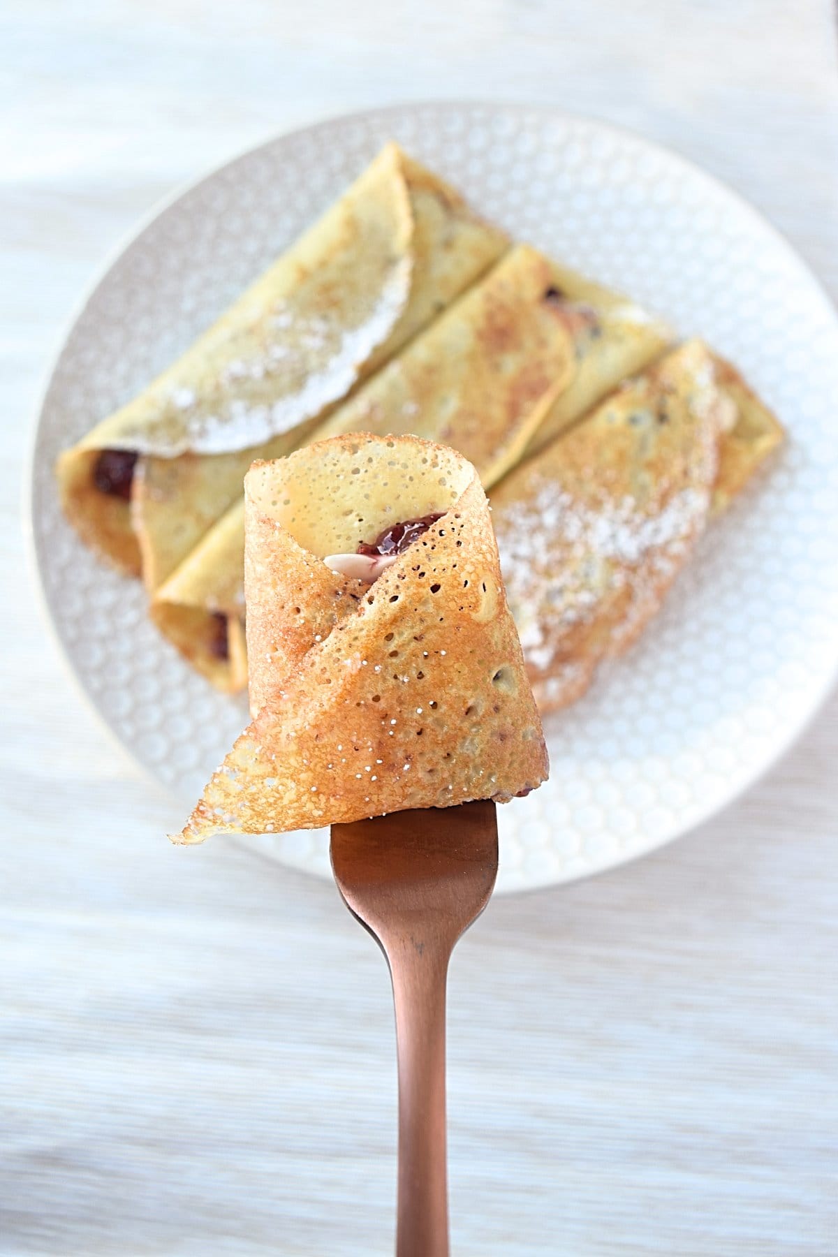 A forkful of gluten free blintzes over a plate of them on the table.