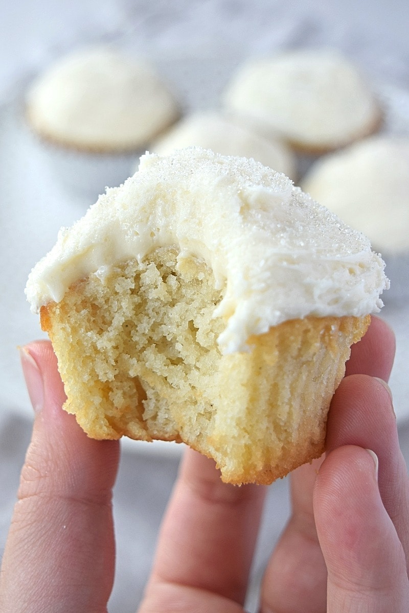 A gluten free vanilla cupcake with a bite taken out of it.