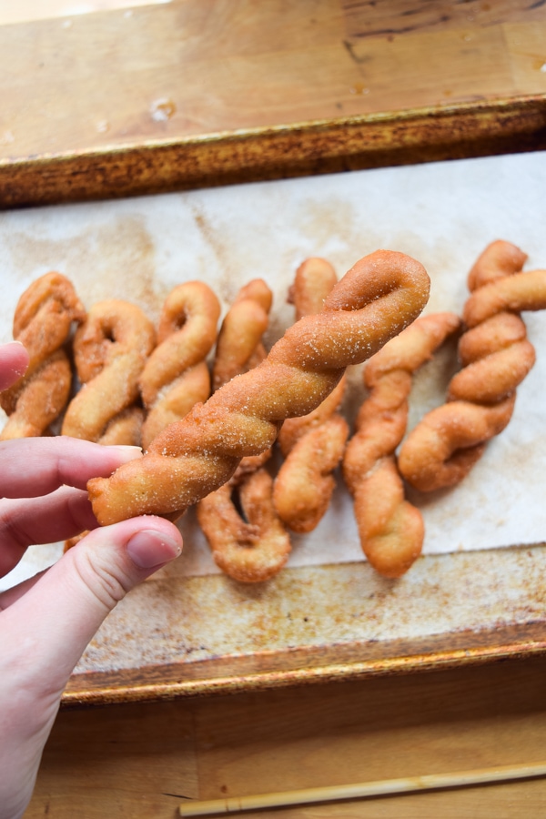 Holding a single cinnamon twist above a tray of cinnamon twists.
