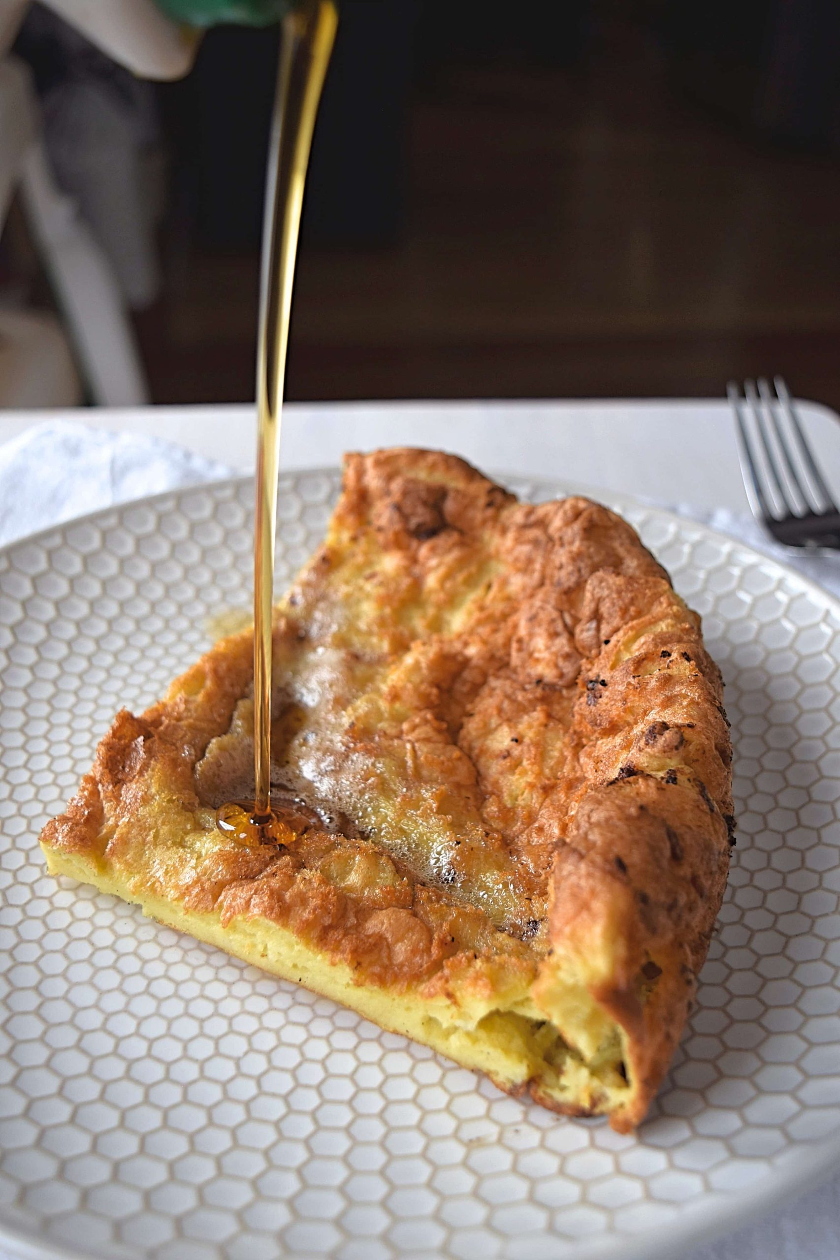 Syrup being poured onto a dutch baby on a white plate.