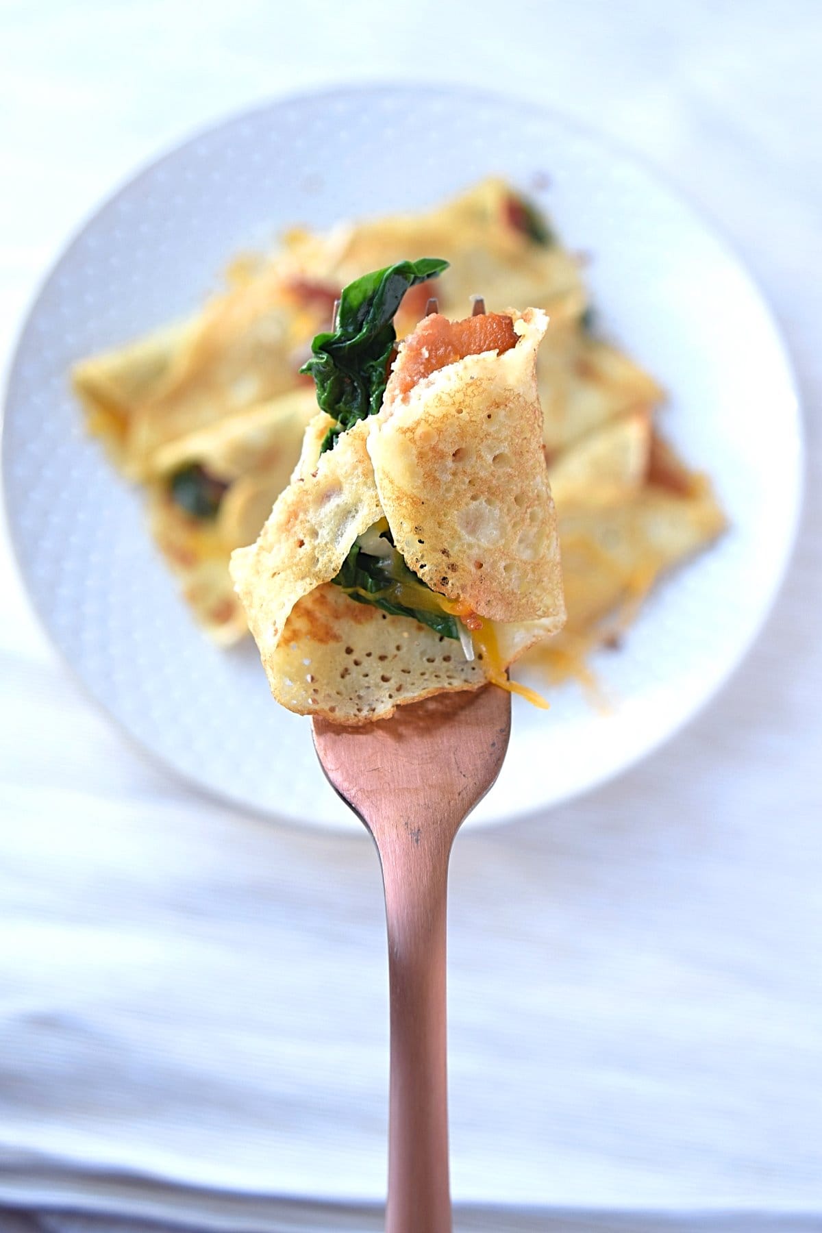 A forkful of savory crepes with bacon, cheese and spinach