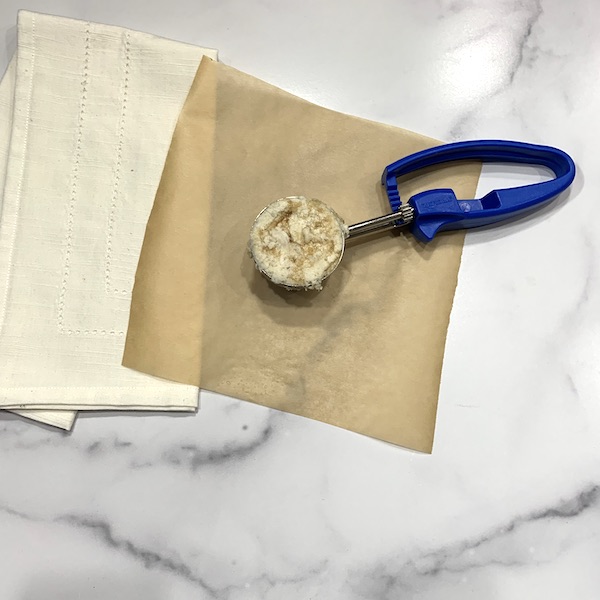 cinnamon roll scone dough in a scoop with a blue handle on top of a piece of parchment paper