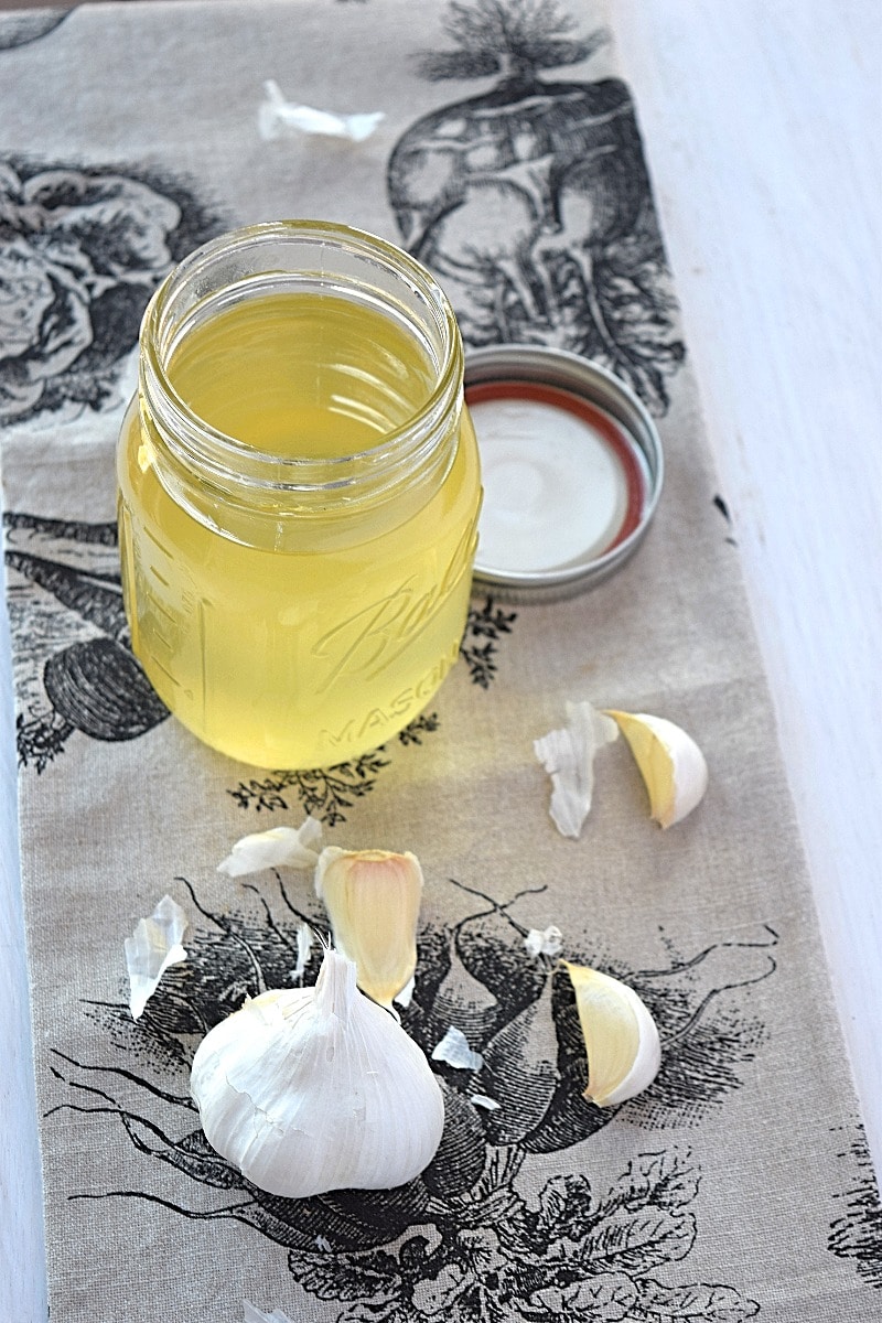 Beauty shot of the garlic oil with the ingredients lying next to it.