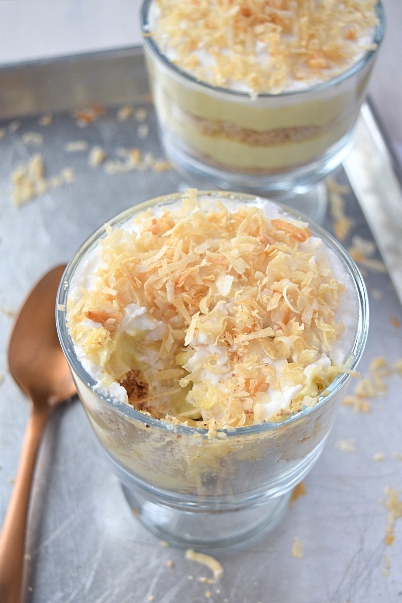 A side view of a glass dish layered with custard and ground nuts, topped with toasted coconut