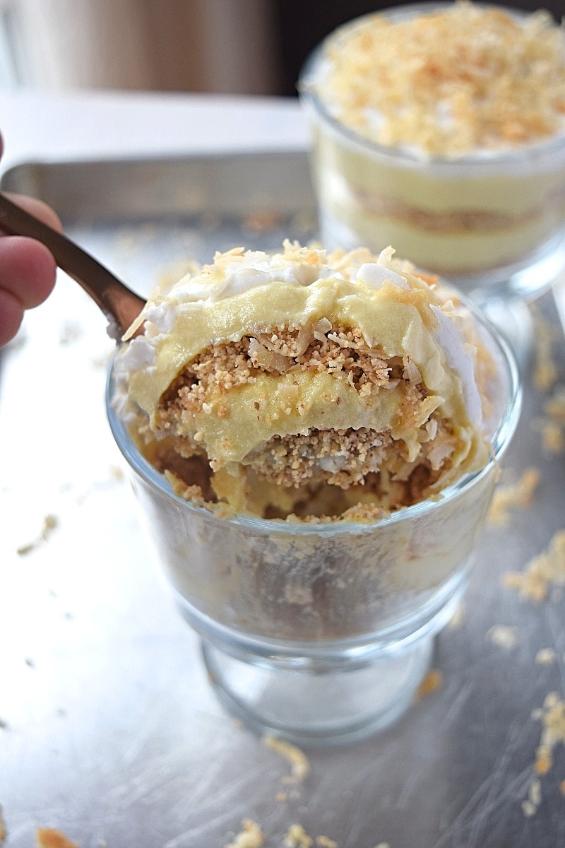A side view of a glass dish layered with custard and ground nuts, topped with toasted coconut