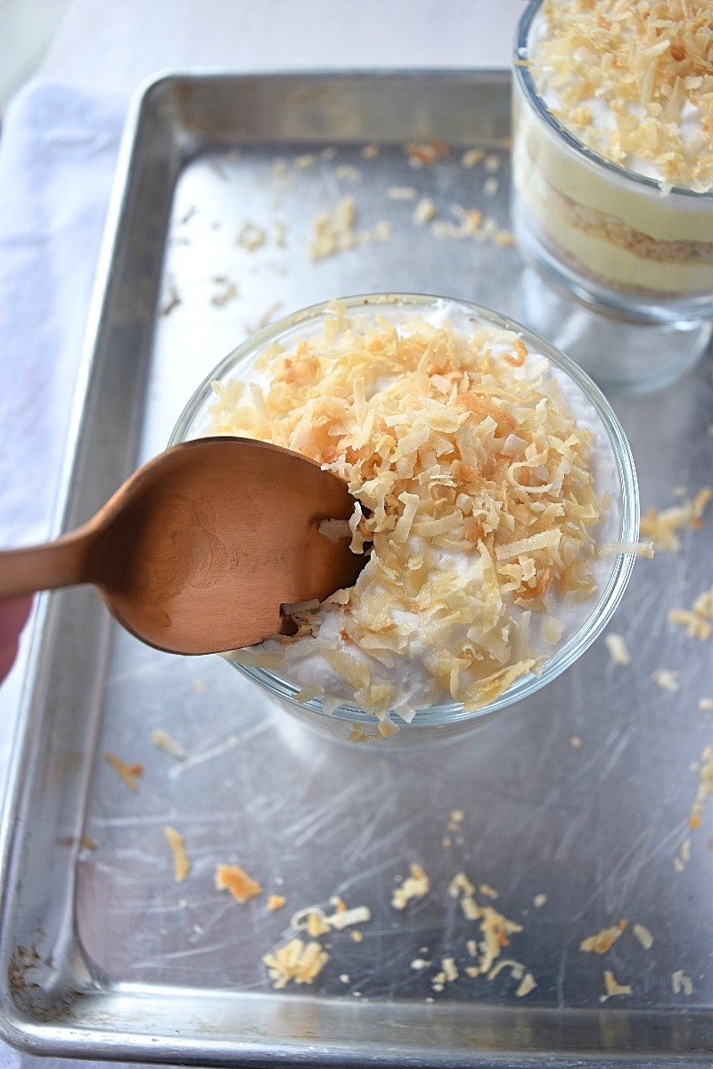 A side view of a glass dish layered with custard and ground nuts, topped with toasted coconut