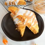 Two freshly baked gluten free pumpkin scones sitting on top of a black plate.
