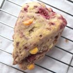 Cover image for gluten free raspberry white chocolate scones - features a single scone cooling on a baking rack