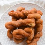 Cover image for Gluten Free Cinnamon Twists blog post. Features a pile of freshly baked cinnamon twists on a white plate.