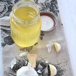 Beauty shot of the garlic oil with the ingredients lying next to it.