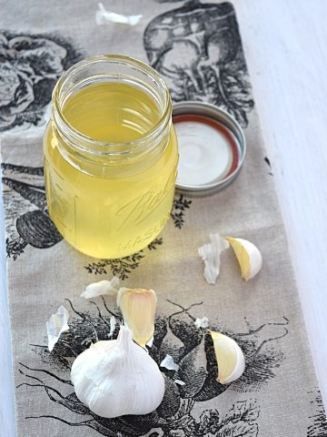 Beauty shot of the garlic oil with the ingredients lying next to it.